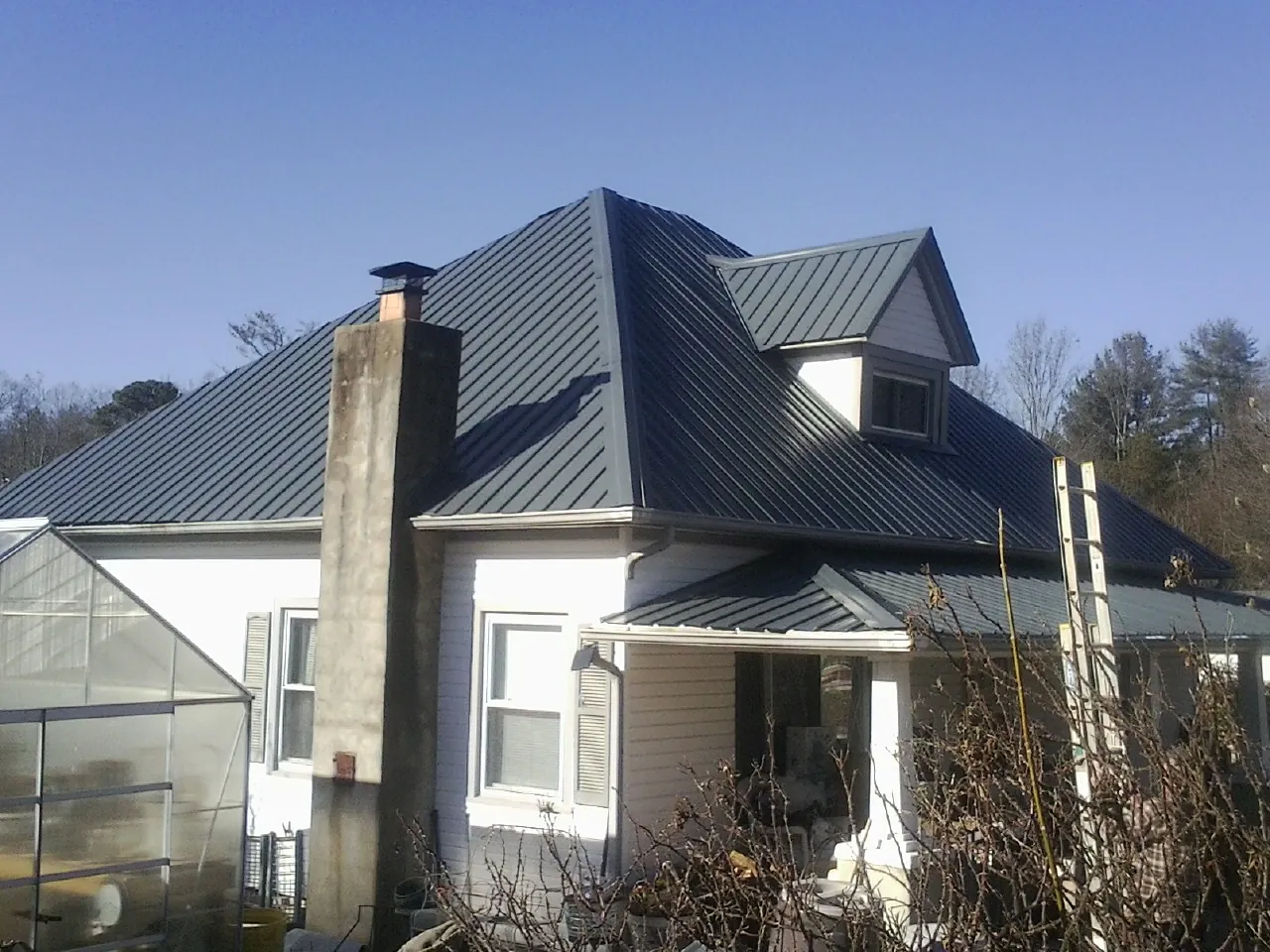 Dark blue standing seam metal roof on a white farmhouse with dormer — Slate & Tile Roof Repair by Roofing Brothers in Waynesville