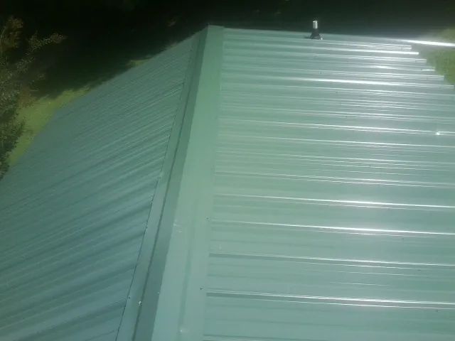 New green metal panels meeting at the ridge of a roof — Flat Roof Repair work by our crew in Waynesville