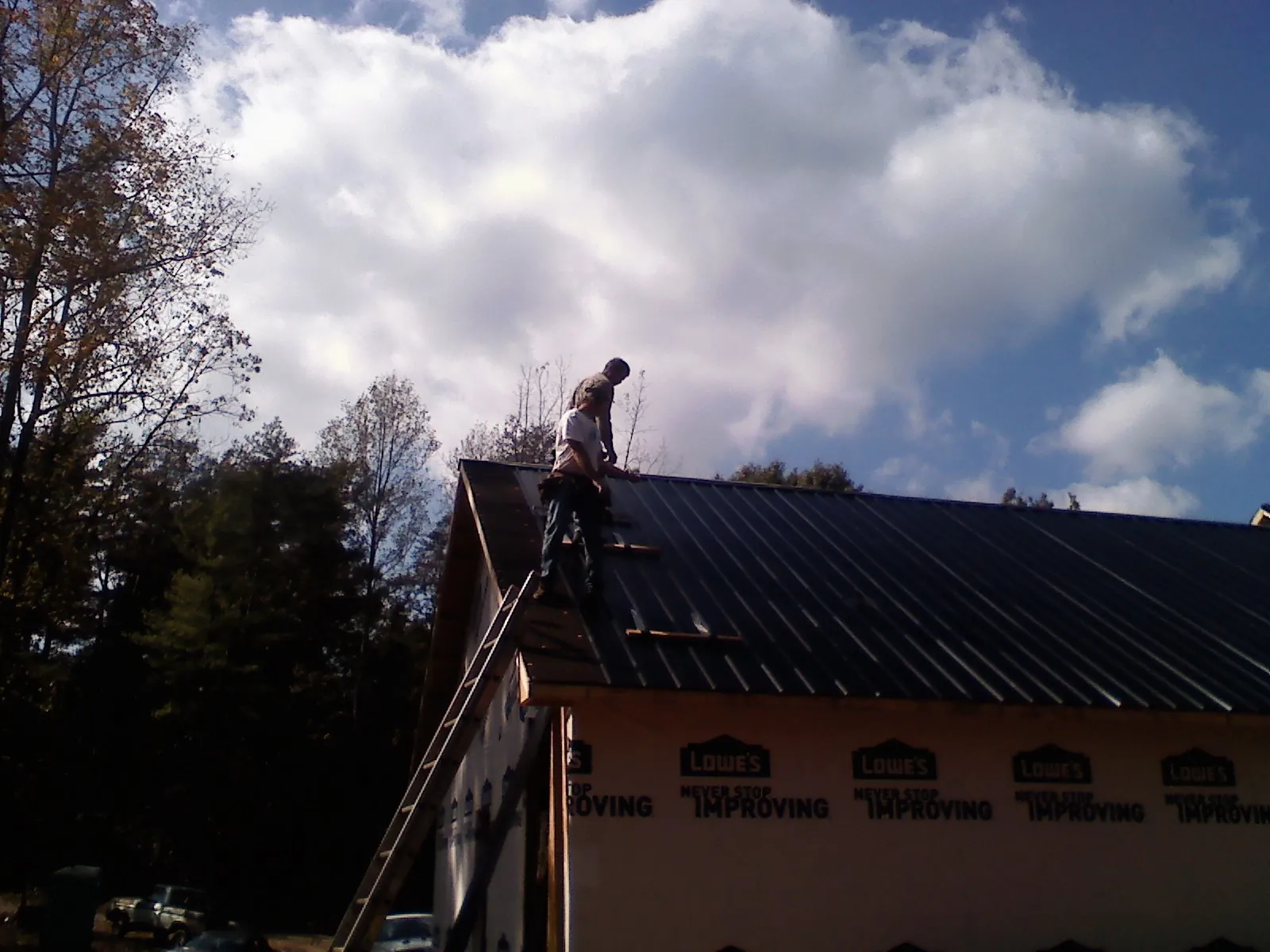 Roofer fastening dark metal panels high against a cloudy sky, from a Roof Inspection job in Waynesville
