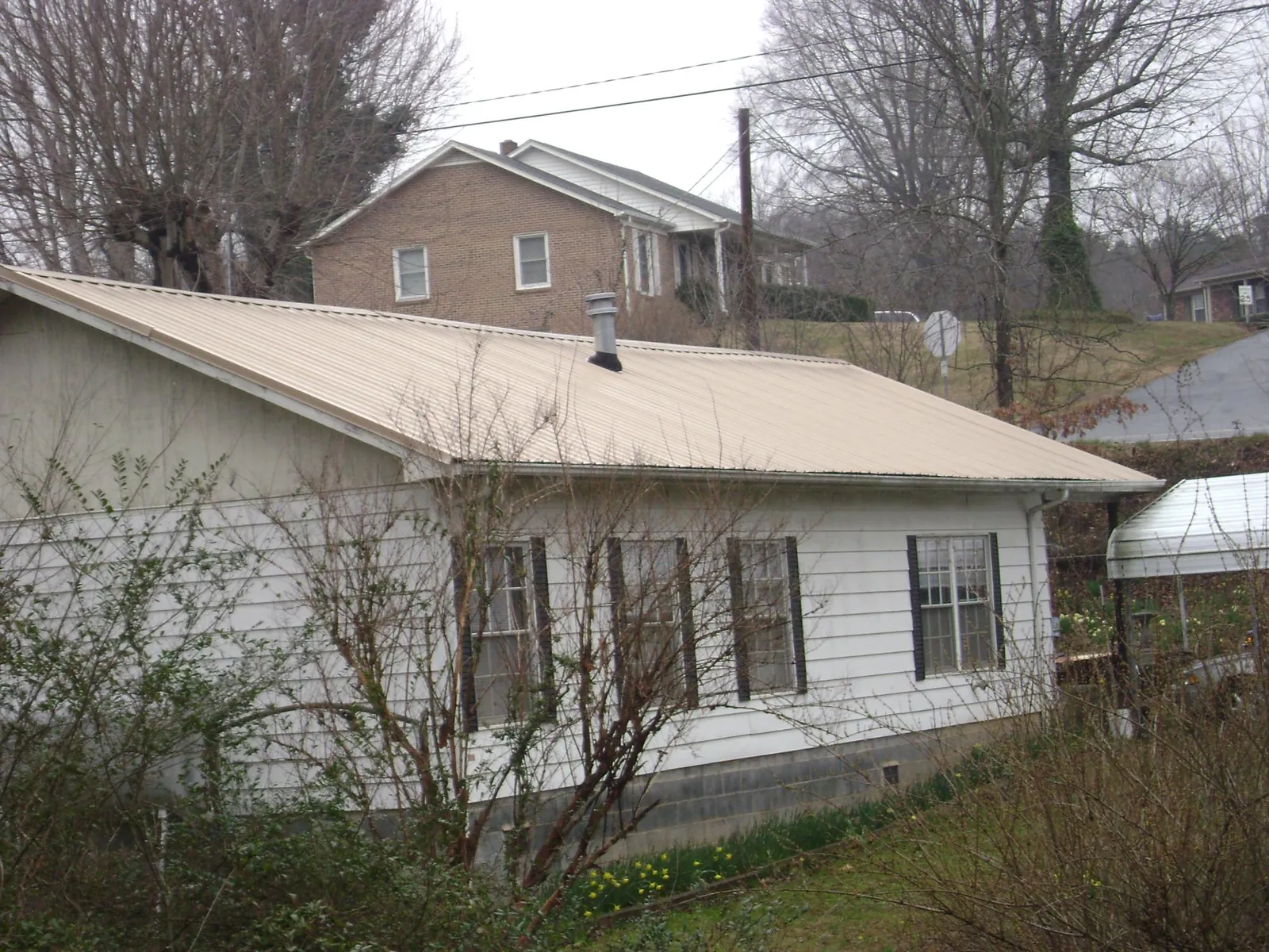 Tan metal roof on a white sided house set into a hillside — Commercial Roofing by Roofing Brothers in Waynesville