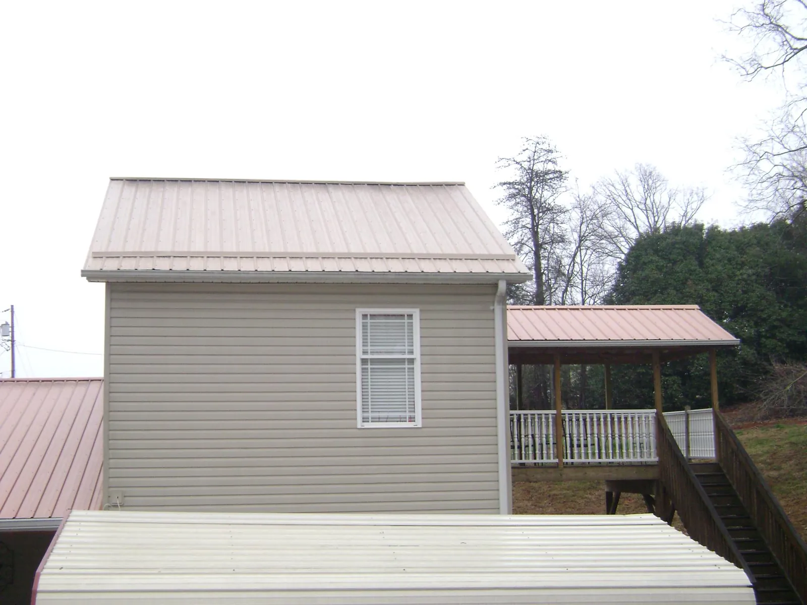 Tan metal roofs on a two story addition and attached porch, from a Roof Replacement job in Waynesville